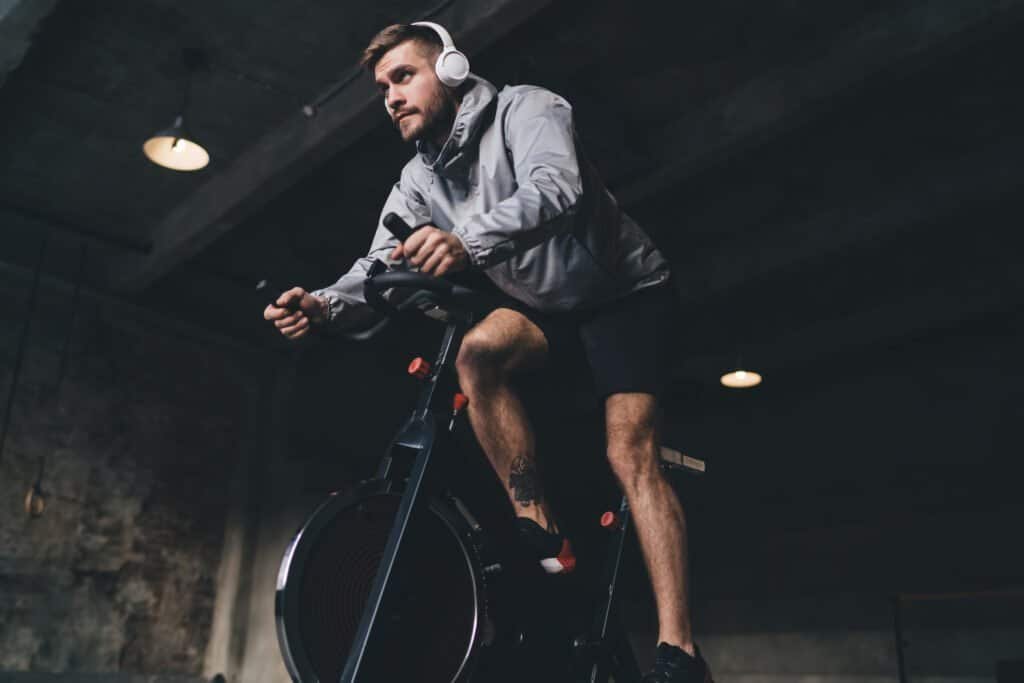 Vitamin D3 Deficiency and Testosterone: Key Facts for Every Man 15 Focused young man training on a stationary bike indoors, wearing headphones, sports attire, and a heart rate monitor.
