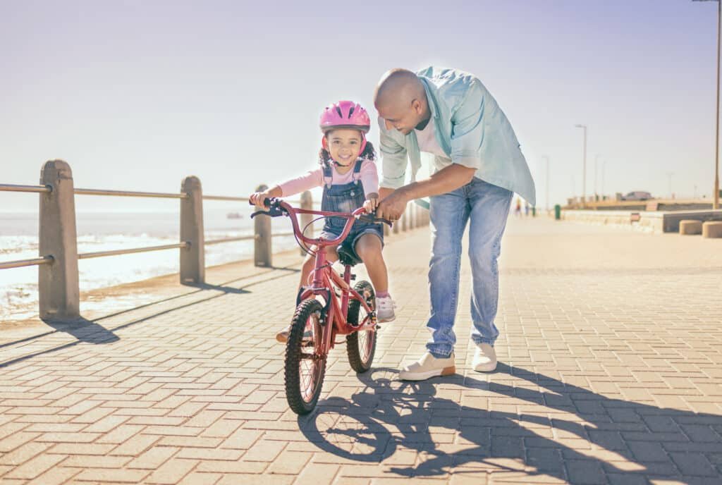 Boron and Beyond: Building Bone Strength in Men Naturally 13 Father helping his daughter ride a bicycle on a sunny day, with the ocean visible in the background.