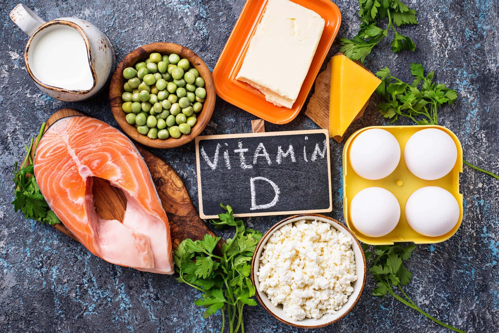 Image of foods with Vitamin D to explain benefits. Variety of vitamin D-rich foods, including salmon, eggs, cheese, peas, milk, and cottage cheese, displayed with a chalkboard labeled 'Vitamin D. Click to learn more. 