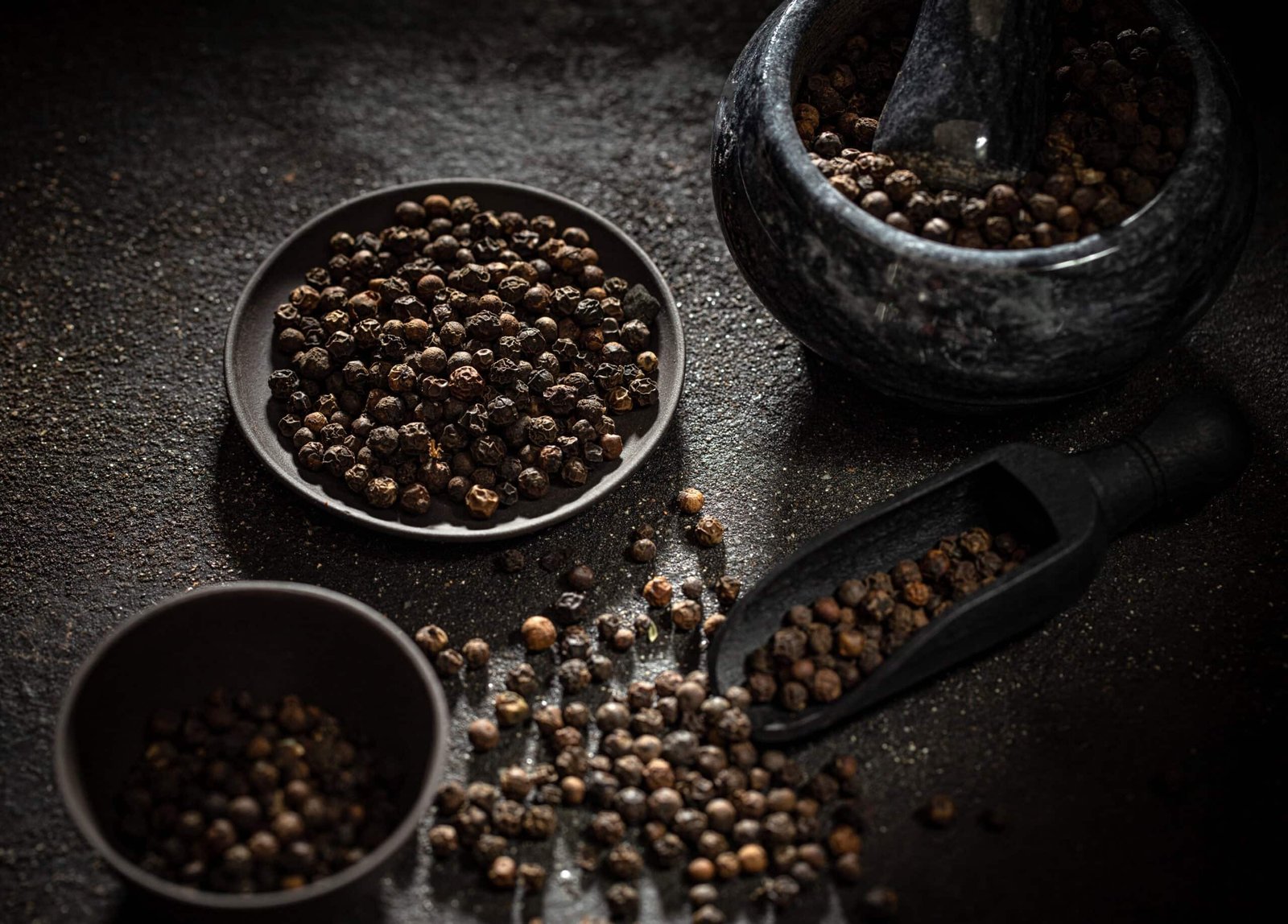 Image for Black Pepper benefits. Black peppercorns in a dish and mortar, with some scattered around on a dark background. Click to learn more. 