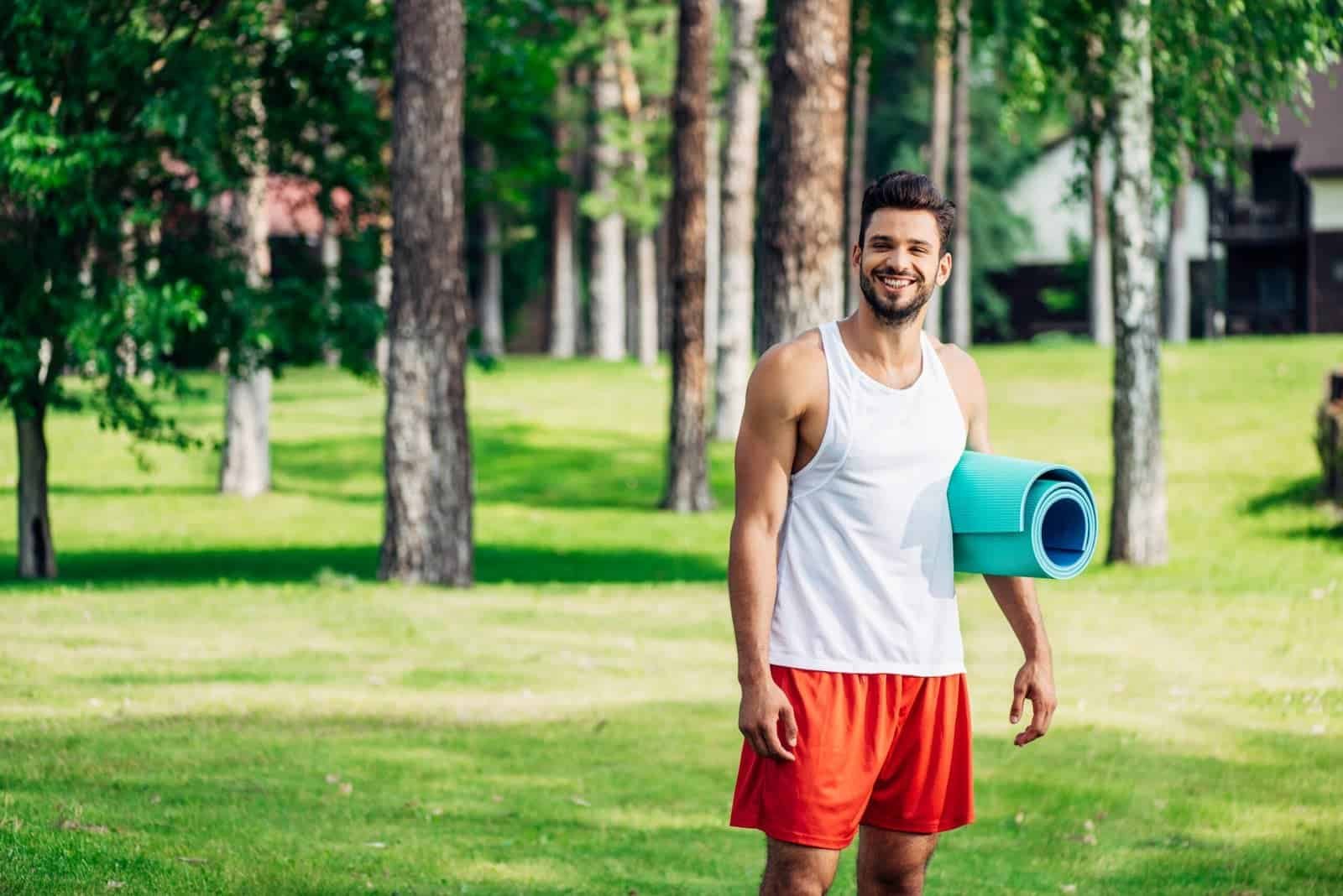 cheerful bearded man holding fitness mat in park 2023 11 27 04 50 06 utc scaled