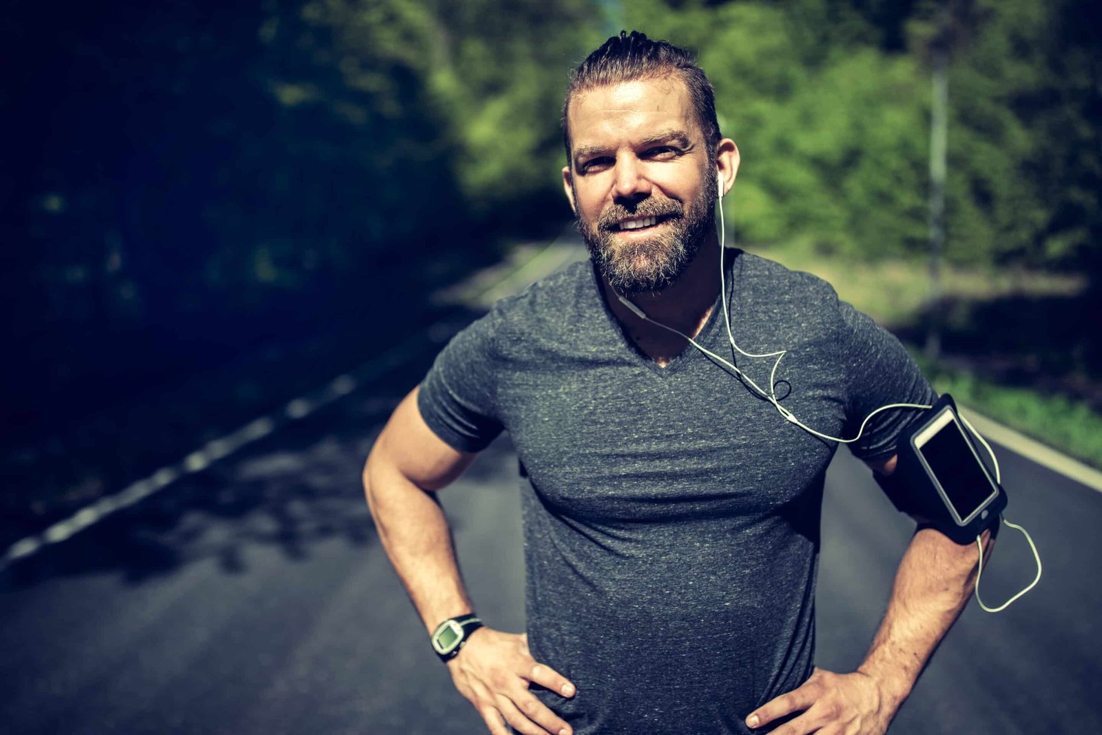 Fit young man smiling while standing with his hands on his hips in the middle of a country road taking a break from his run - how to improve body composition