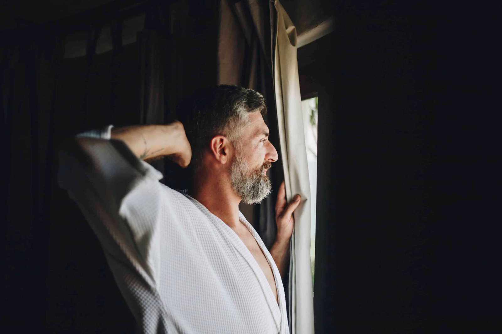 a man in a robe looking out a window thinking about melanin vs melatonin