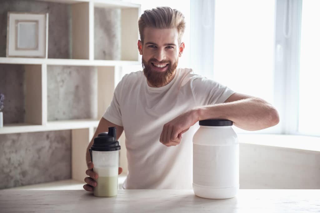 Before and After Creatine Benefits: 7 Transformations You Can Expect 5 A young white man at kitchen counter and just mixed a protein shake with creatine benefits. Room is bright and sunny.