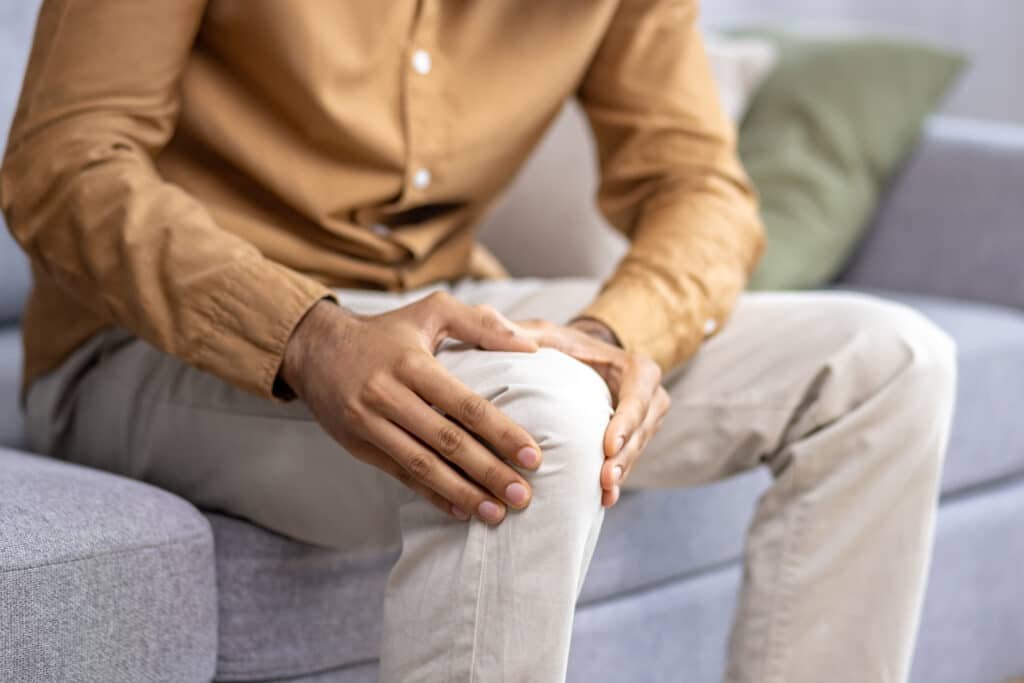 The Role of Boron in Healing Aching Joint Pain 3 A man sitting on a couching rubbing his knee due to aching joint pain. Could supplementing with Boron improve this aching joint pain?