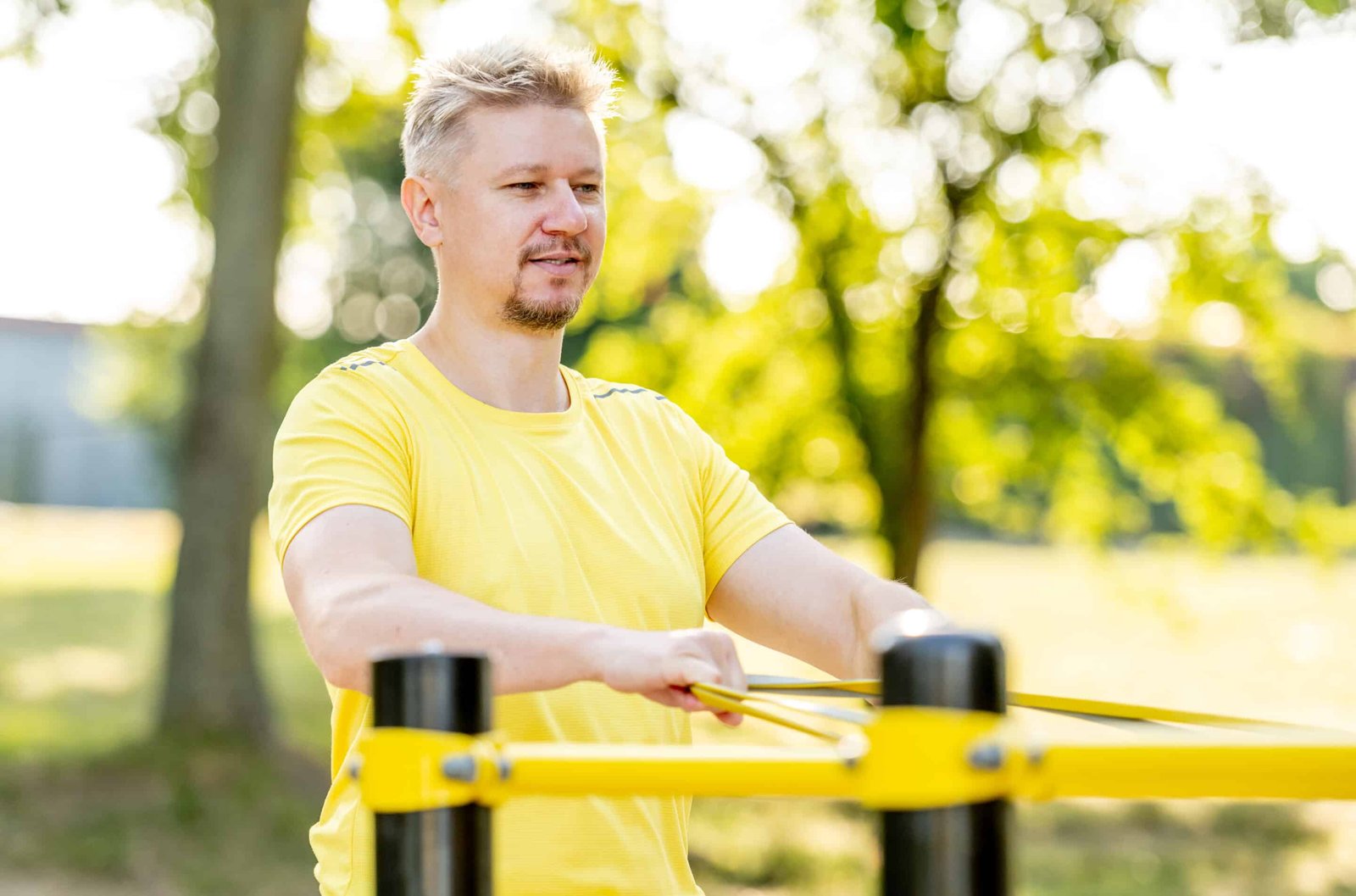 Man exercising with elastic rubber band outdoors making arm workout. Guy making gains with supplements for men over 40.