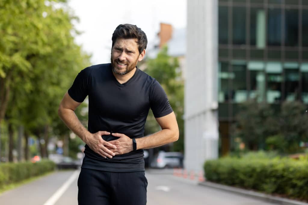 Digestive Health Supplements: A No-Fluff Guide to Gut Optimization 17 A young male athlete stands on the street and holds his stomach with his hands, suffering and hiding from pain. He is in need of digestive health supplements.