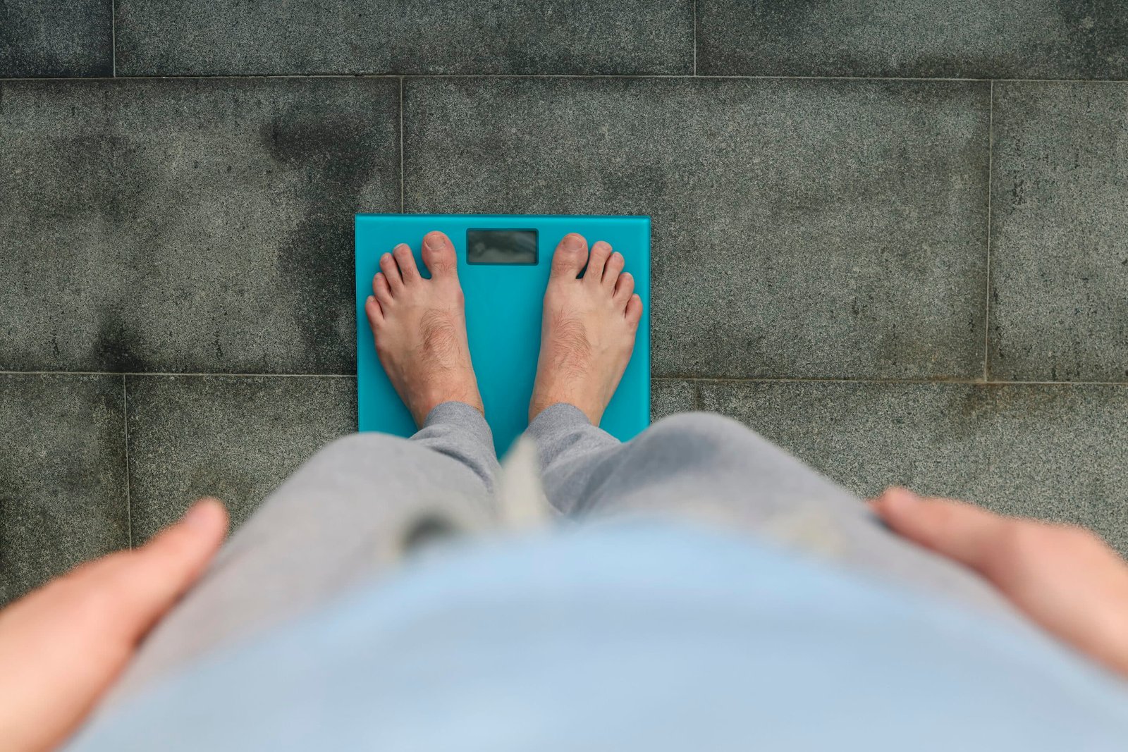 A heavier man standing on a scale with perception from the view of him looking down at increased weight, wondering How Hormones affect wright loss.