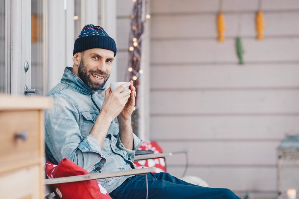 5 Ways to Calm Your Nerves with Deep Breathing Techniques 5 Positive glad attractive male model holds cup of tea, has good rest at balcony, breathes fresh air and enjoys sunny weather, has pleasant smile on face, feels delighted and pleased. Calm Your Nerves article for Men by Adaptafy.